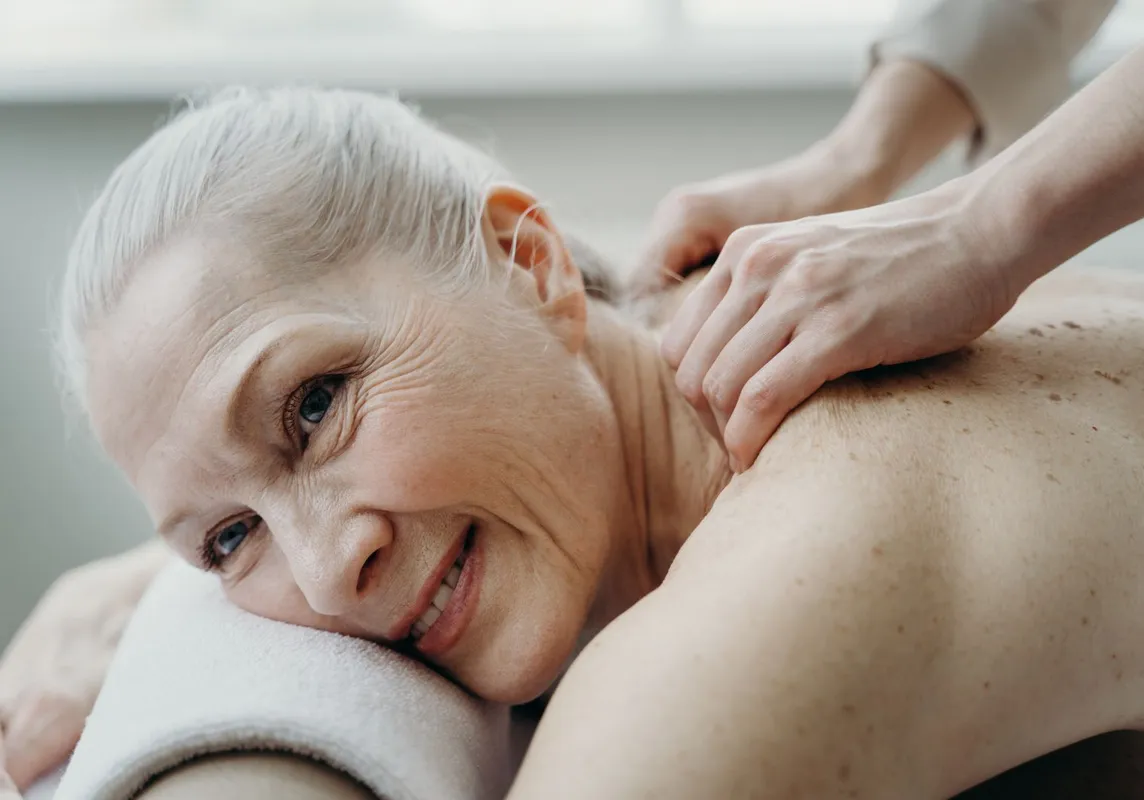 Eine lächelnde Seniorin genießt eine sanfte Massage.